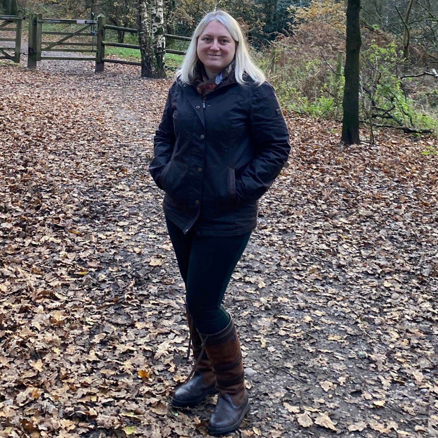 A woman wearing a Mountrath Wax Jacket in a forest in an autumnal setting with brown leaves littering the floor.//© Outdoor & Country