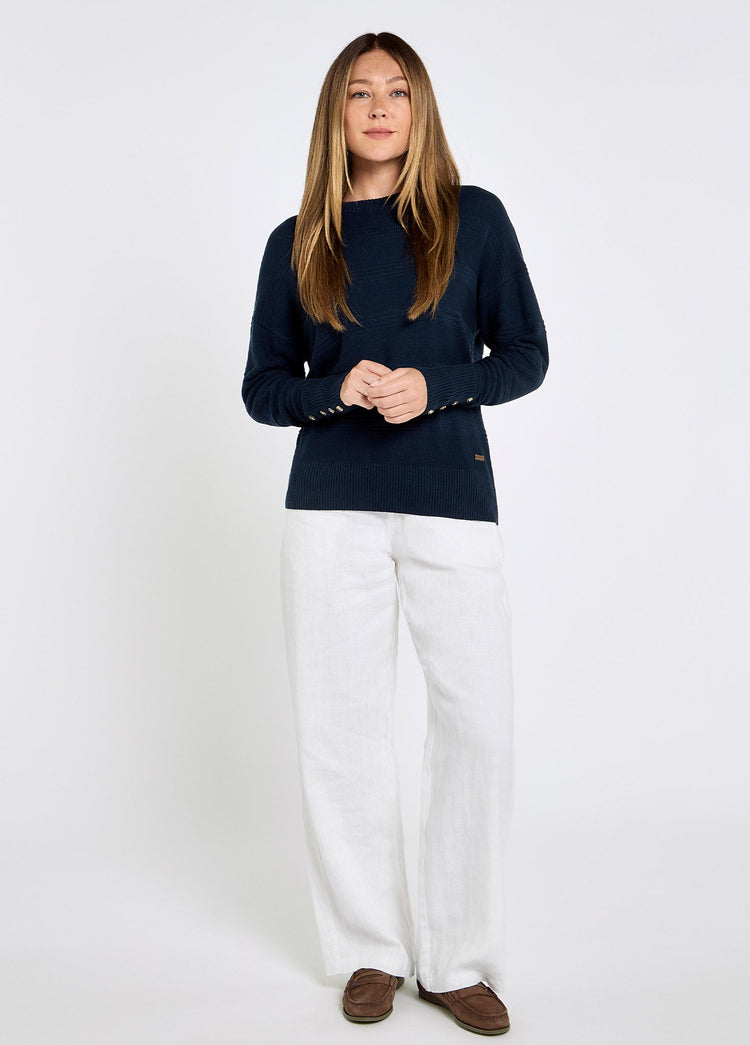 Vrouw in donkerblauwe damestrui van bamboe-, Tencel- en kasjmiermix met witte linnenbroek en bruine bootschoenen