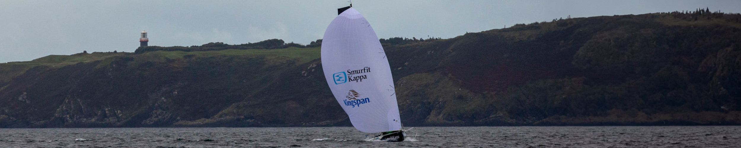 Wide image of Tom Dolan on his boat off the Irish coast with a lighthouse on the land close to the sea.